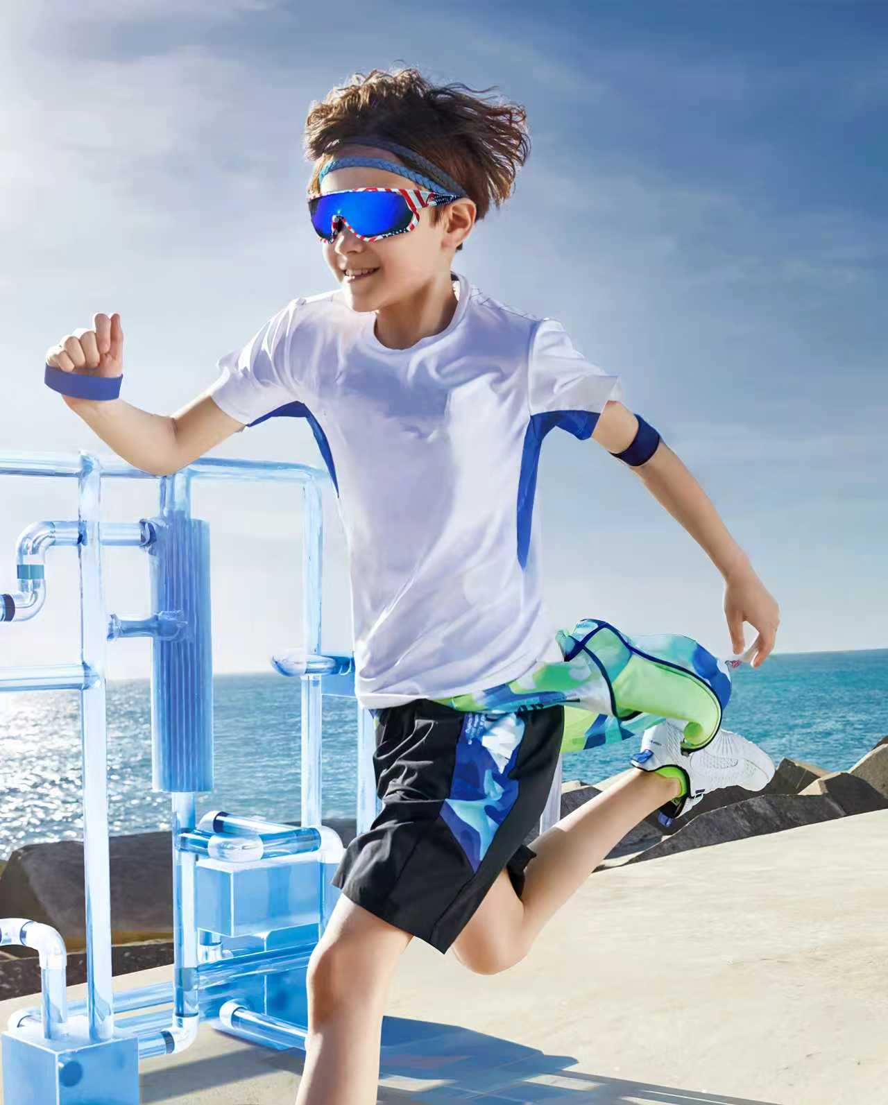 Child running on a deck with ocean view wearing sunglasses and athletic gear.